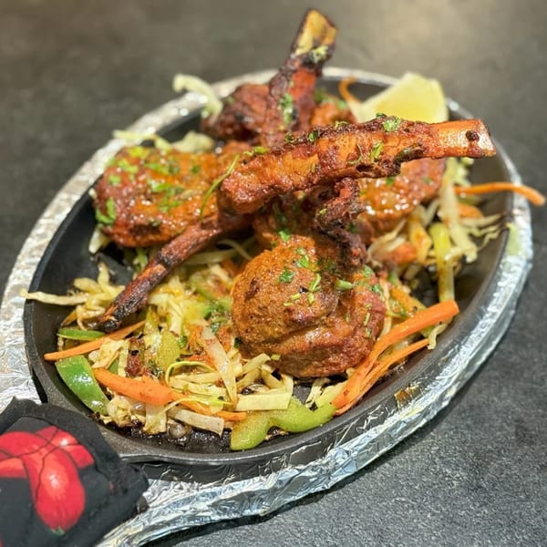 Indian lamb chops and meatballs with sautéed vegetables on a sizzling platter, garnished with cilantro and lemon.
