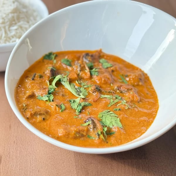 A white bowl of Amrut's Indian curry, garnished with fresh cilantro, with a side of rice.