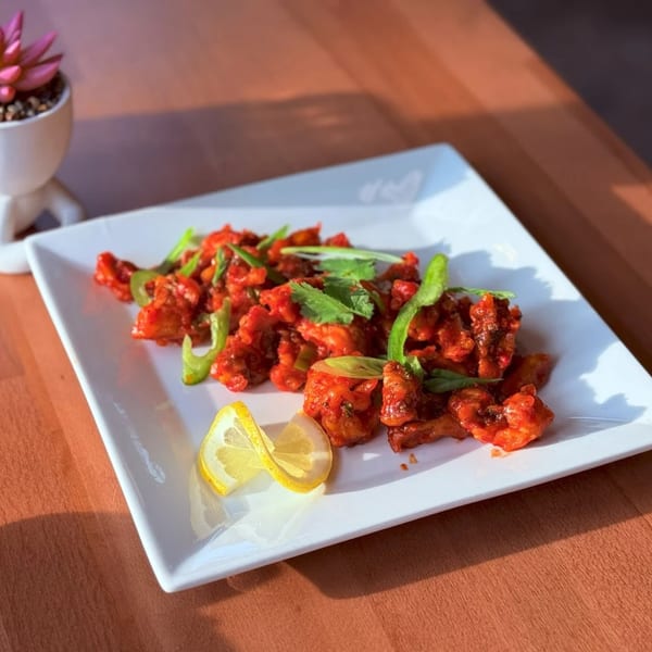 Amrut: Taste of India's red chili chicken, garnished with green peppers, cilantro, and lemon wedges.