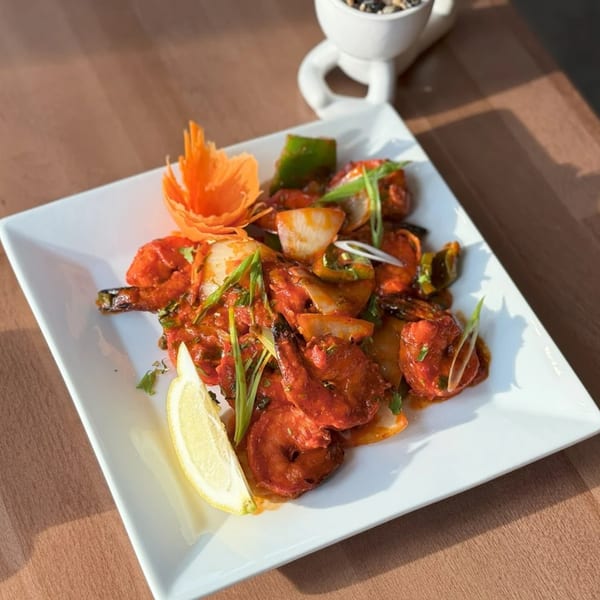 Indian chili shrimp with onions, peppers, and a lemon wedge on a white plate.