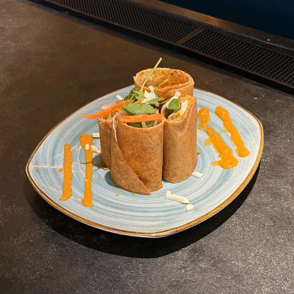 Indian spring rolls with vegetables and cilantro, drizzled with orange sauce on a blue plate.